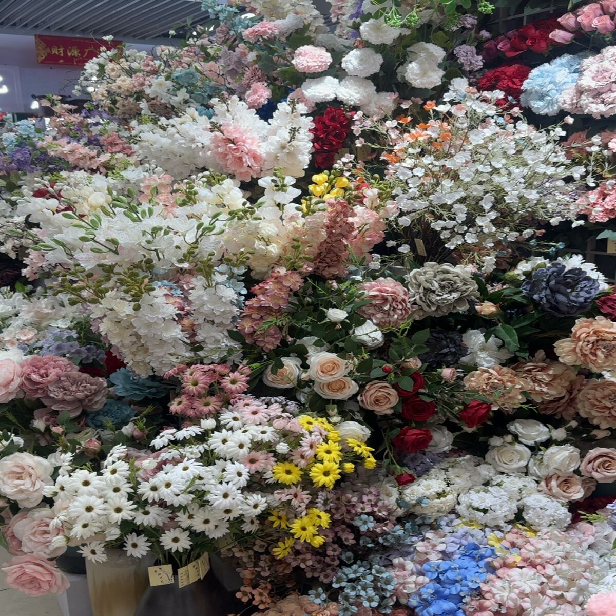 Mixed artificial flower arrangements including daisies, peonies, and roses.