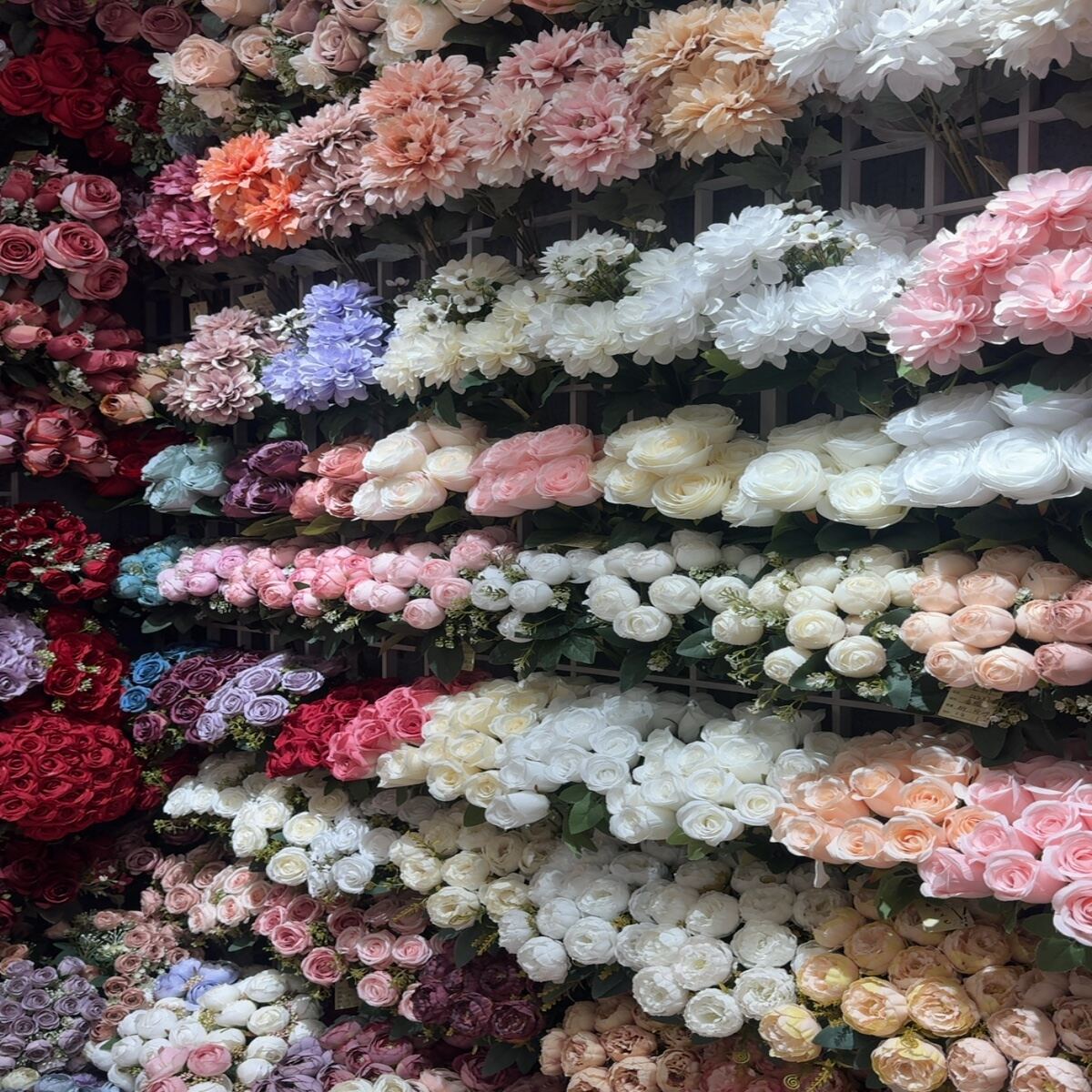 Assortment of artificial roses, peonies, and mixed flowers in various colors on display.